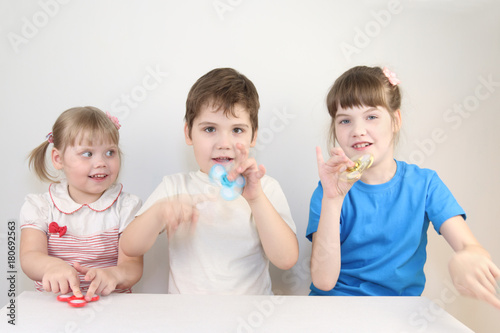 Three happy children play with spinners on table in white studio