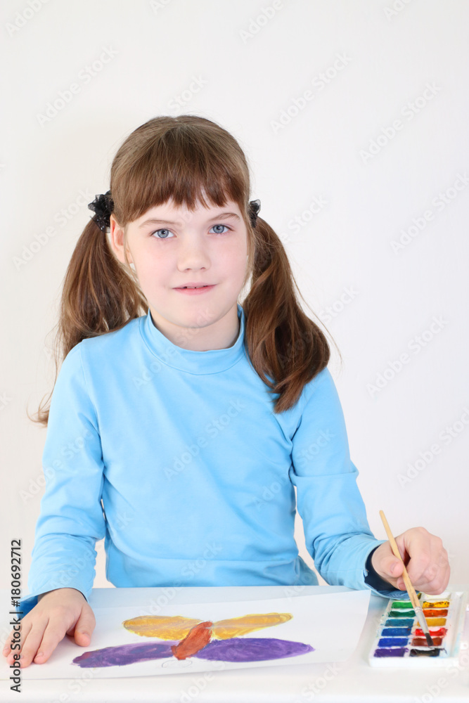 Smiling pretty girl paints watercolor butterfly on table in white room Smiling pretty girl paints watercolor butterfly on table in white room