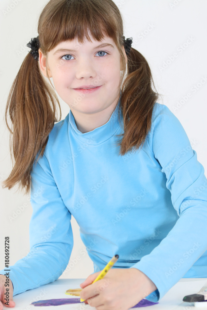 Smiling girl paints watercolor butterfly with pencil on table in white room Smiling girl paints watercolor butterfly with pencil on table in white room