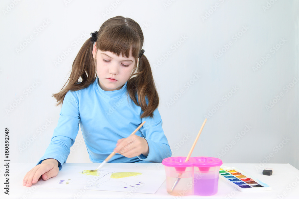 Pretty girl in blue watercolor paints butterfly on table in white room Pretty girl in blue watercolor paints butterfly on table in white room