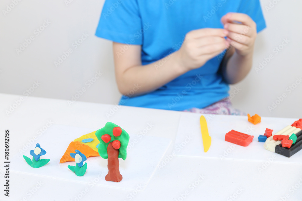 Girl hands molding house, tree, flowers from plasticine on table in room Girl hands molding house, tree, flowers from plasticine on table in room
