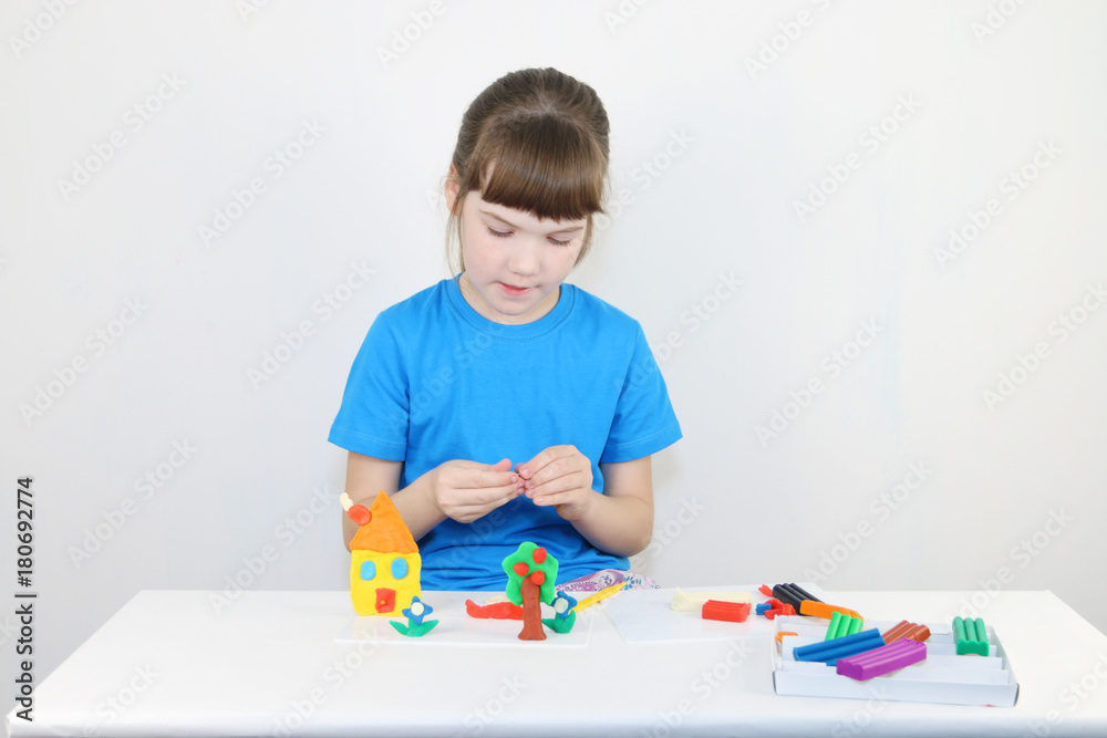 Pretty girl in blue molds house from plasticine on white table in white room Pretty girl in blue molds house from plasticine on white table in white room