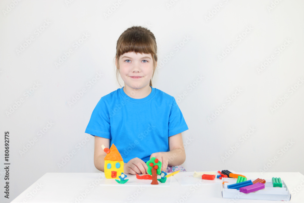 Smiling girl in blue molds house from plasticine on white table in white room Smiling girl in blue molds house from plasticine on white table in white room