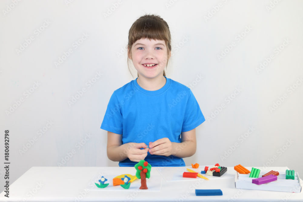 Happy girl in blue molds from plasticine on white table in white room Happy girl in blue molds from plasticine on white table in white room