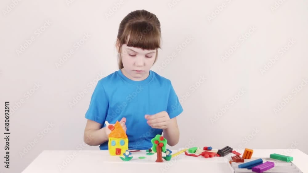 Girl in blue molds house from plasticine on white table in white room, time lapse
Girl in blue molds house from plasticine on white table in white room, time lapse