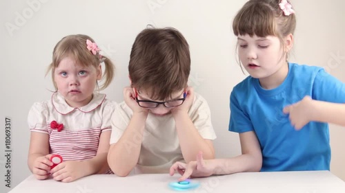 Three happy children play with spinners on table in white studio