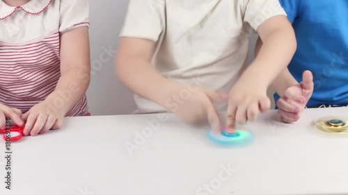 Hands of three children playing with spinners on table in white studio
