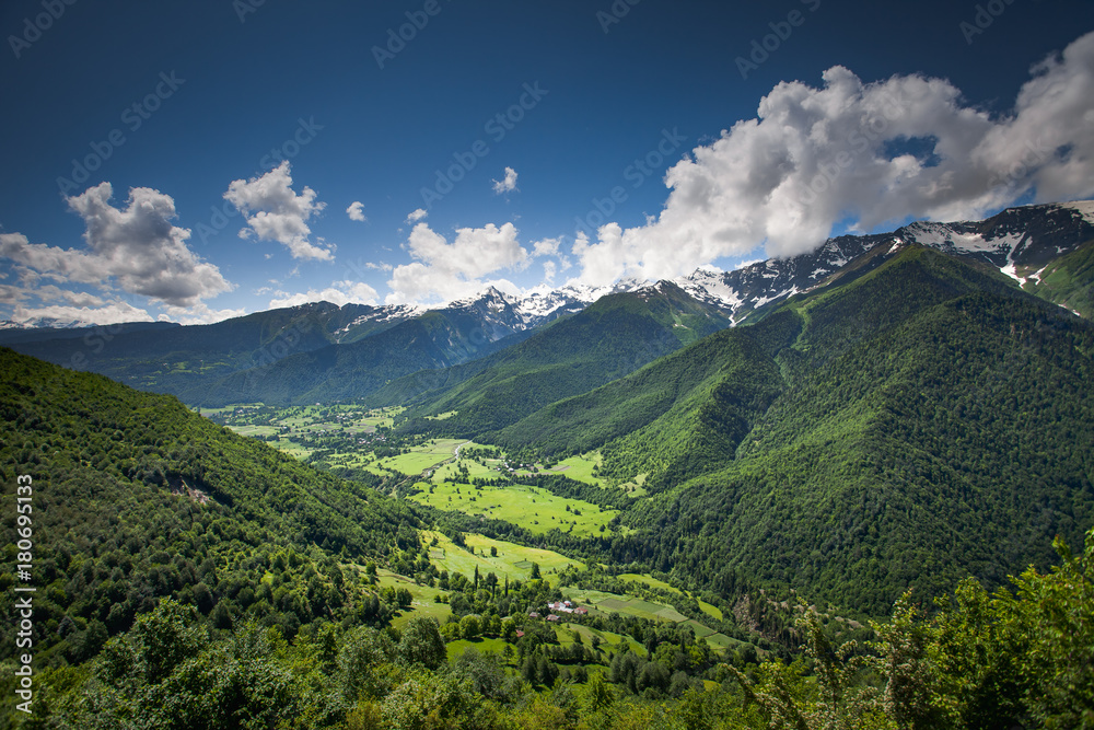 Fototapeta premium Panoramic summer landscape with green hill and mountain snow capped peak against blue cloudy sky. Svanetia region, Georgia. Main Caucasian ridge. Travel background. Holiday, hiking, sport, recreation