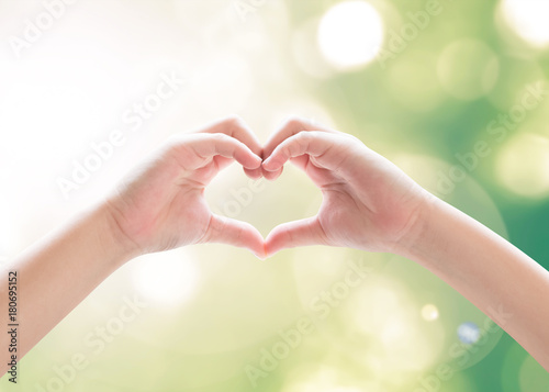 Heart-shape hand gesture of kid s body language for children s love  peace  kindness and world humanitarian aid concept. Hand isolated on sky with green bokeh and sun flare