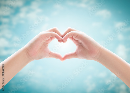 Heart-shape hand gesture of kid's body language for children's love, peace, kindness and world humanitarian aid concept. Hand isolated on blur blue sky with cloud © Chinnapong