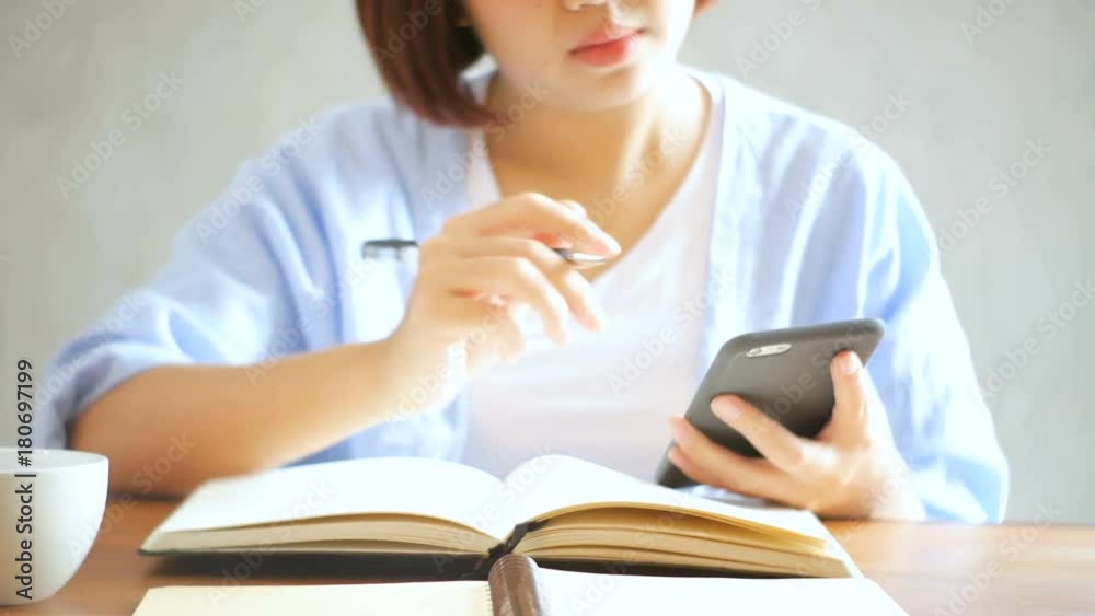 Young business woman in white dress sitting at table in cafe and writing in notebook. Asian woman talking smartphone and cup of coffee. Freelancer working in coffee shop. Student learning online. Young business woman in white dress sitting at table in cafe and writing in notebook. Asian woman talking smartphone and cup of coffee. Freelancer working in coffee shop. Student learning online.