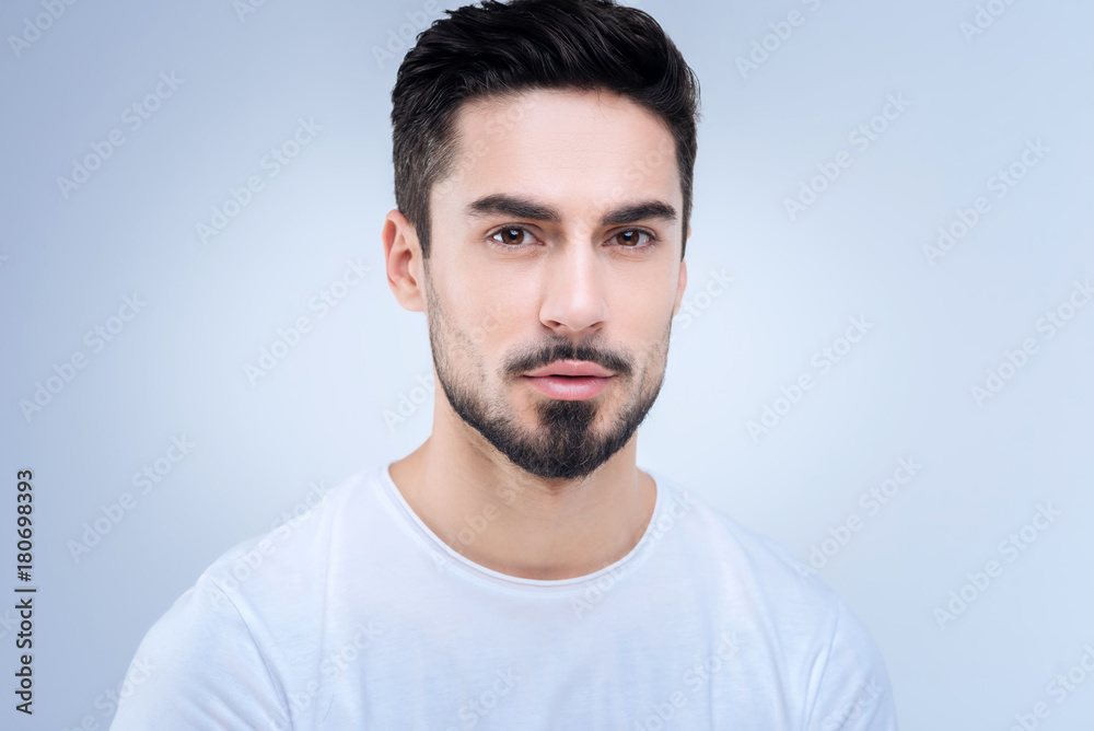 Fototapeta premium Calm. Bearded handsome young man looking calm and peaceful while standing against the blue background and looking straight