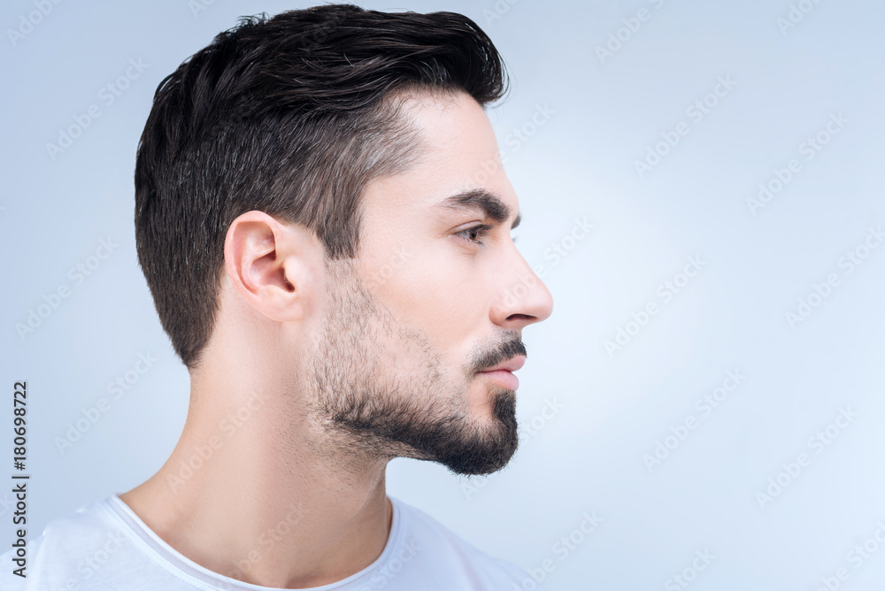 Fototapeta premium Nice haircut. Calm unemotional young man standing quietly and showing his new haircut after visiting a qualified barber