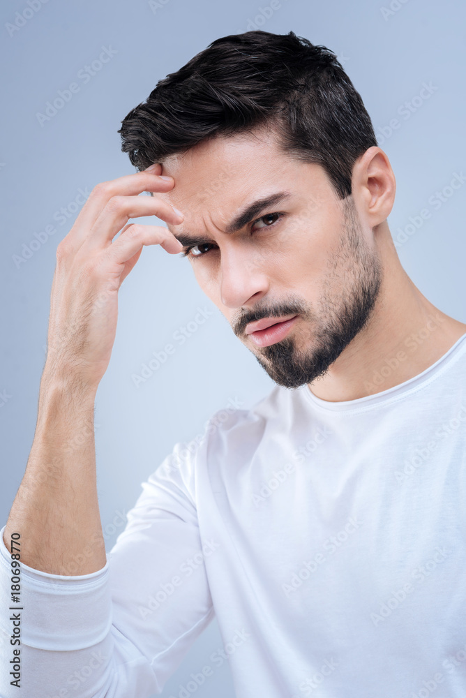Grey thoughts. Upset serious man frowning and touching his forehead while thinking about making a difficult and unpleasant decision Grey thoughts. Upset serious man frowning and touching his forehead while thinking about making a difficult and unpleasant decision