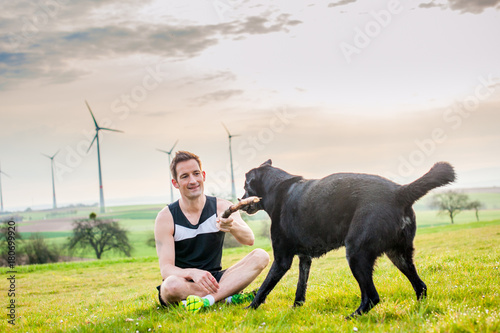 Young man sits on the field with a labrador, at sunset with a view of the windmills © Pavel