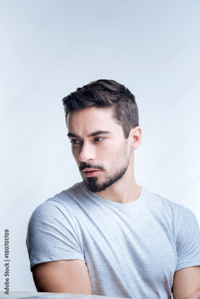 Gloomy mood. Sad handsome young man sitting quietly against the blue background while being unhappy after hearing unpleasant news Gloomy mood. Sad handsome young man sitting quietly against the blue background while being unhappy after hearing unpleasant news