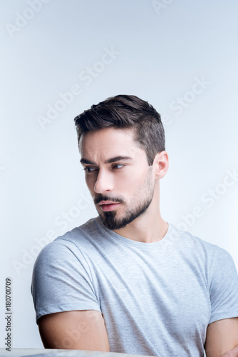 Gloomy mood. Sad handsome young man sitting quietly against the blue background while being unhappy after hearing unpleasant news