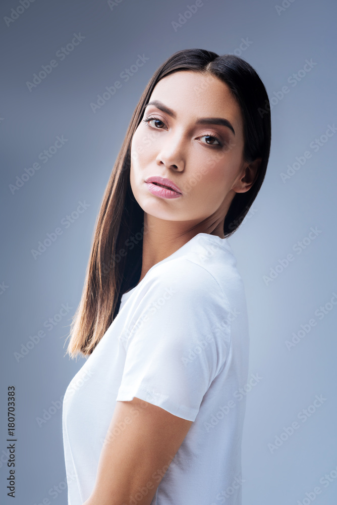 Straight back. Calm beautiful young woman standing against the blue background with a straight back and looking seriously into the distance Straight back. Calm beautiful young woman standing against the blue background with a straight back and looking seriously into the distance
