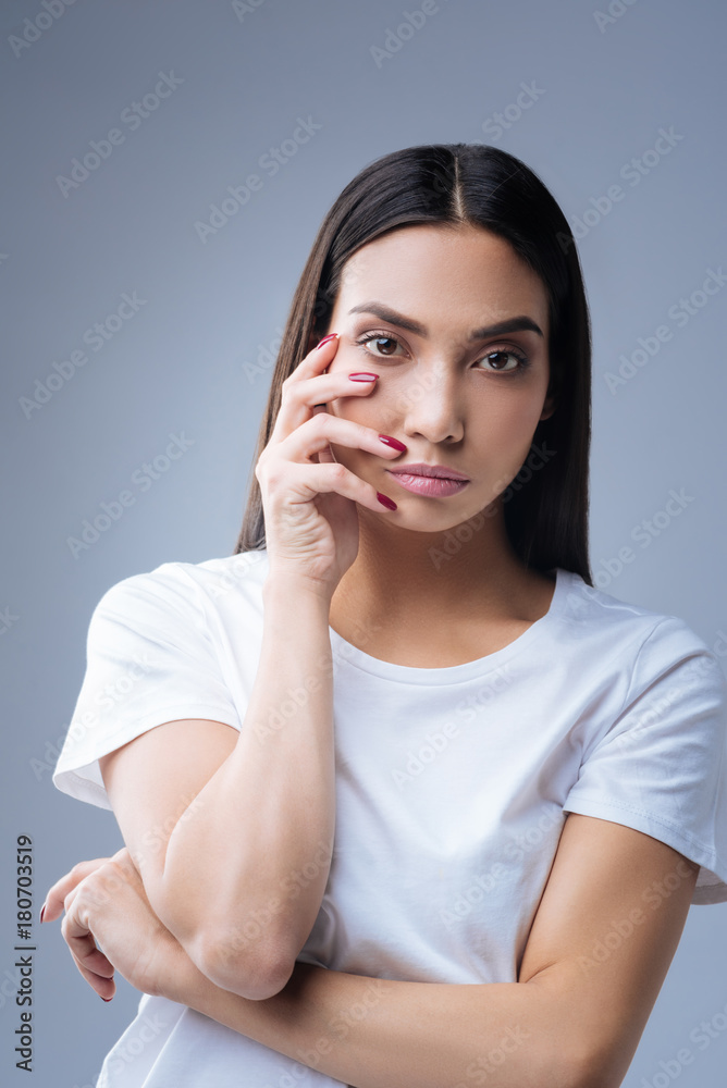 Nail designer. Calm beautiful nail designer standing against the blue background with her fingers touching her right chick while waiting for the clients to visit her Nail designer. Calm beautiful nail designer standing against the blue background with her fingers touching her right chick while waiting for the clients to visit her
