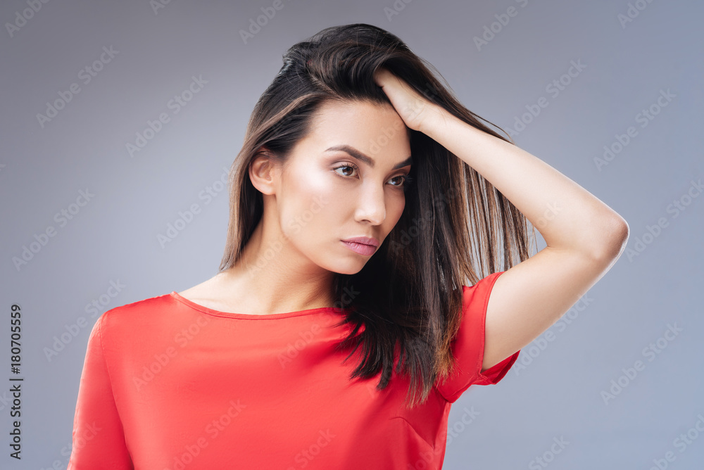 Fototapeta premium Wet hair. Emotional young woman looking unsatisfied while standing against the blue background and touching her wet hair after the rain