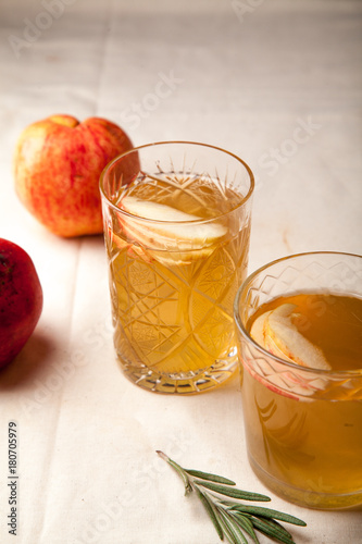 Two vintage glasses with apple cider on black background. Christmas beverages concept. Two red apples and rosemary sprig aside. Warm backlight. Vertical composition.