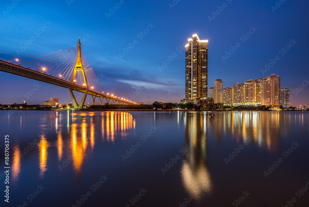 Fototapeta premium Bhumibol Bridge, Industrial Ring Road Bridge z wieżowcem w scenie nocnej po zachodzie słońca. Zmierzch nieba i odbicia światła na gładkiej wodzie, Tajlandia