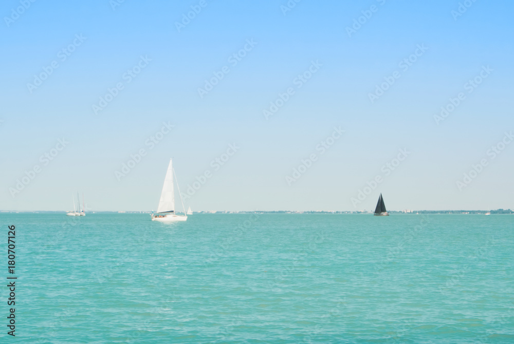 Fototapeta premium Bright blue transparent lake river water with white and black yachts at the horizon on sunny summer day.