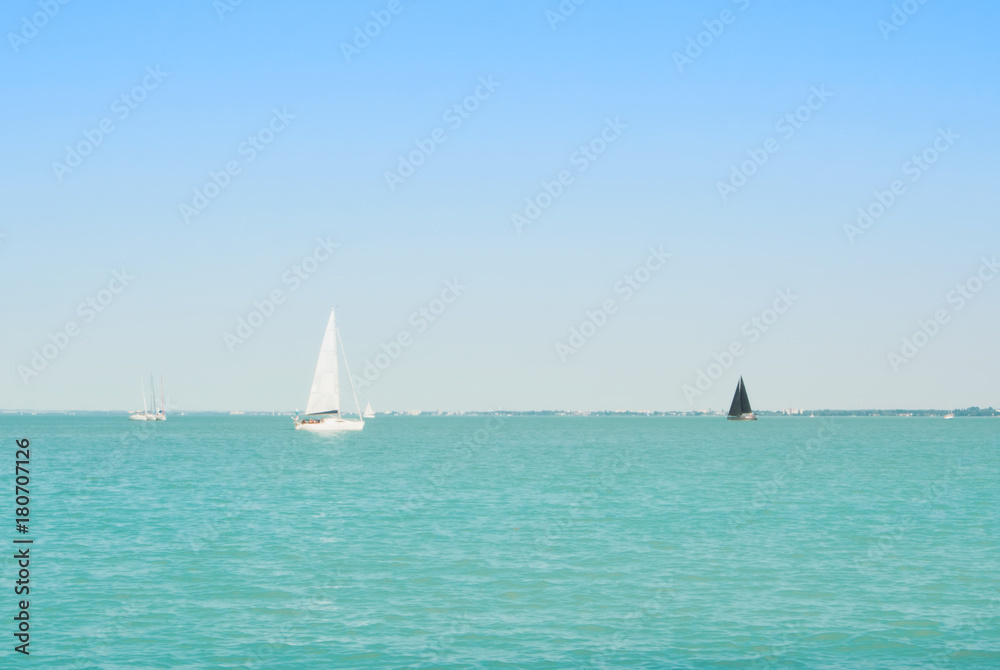 Bright blue transparent lake river water with white and black yachts at the horizon on sunny summer day.