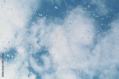 Water drops on a window glass, a blue cloudy sky at the background. © Victoria