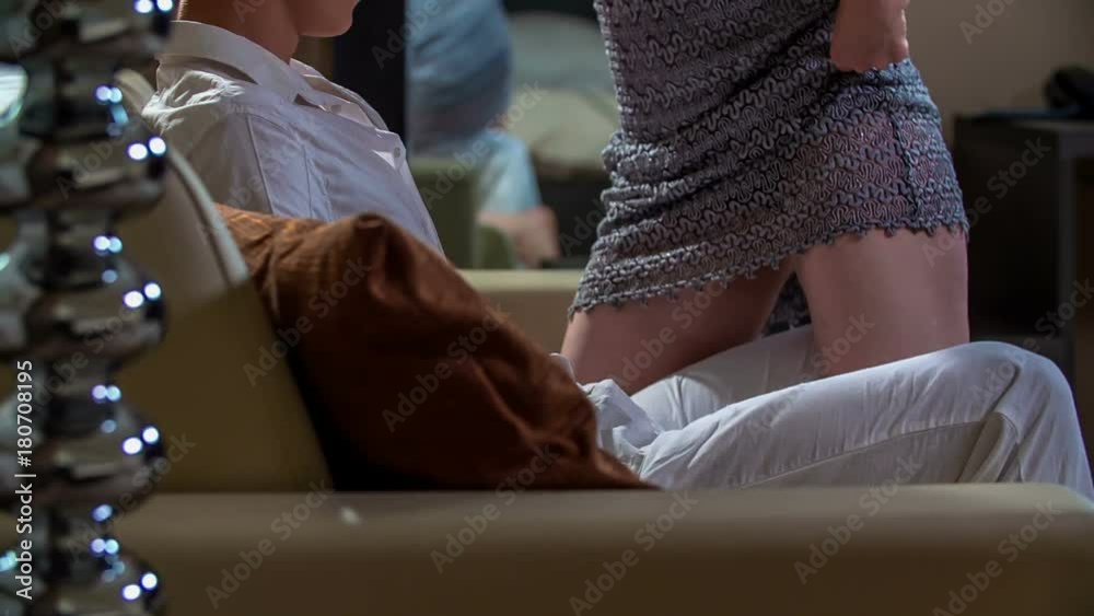 A young woman is lifting up her skirt and she is sitting down on her boyfriend's lap and he is sitting on a couch.