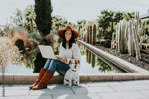 .Pretty young woman working outdoors with her adorable dog jack rusell in a park surrounded by cactus and a small pond. photo