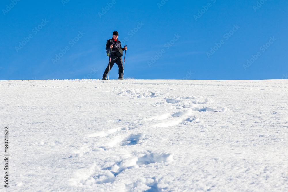 Man is snowshoe hiking through deep snow on sunny day