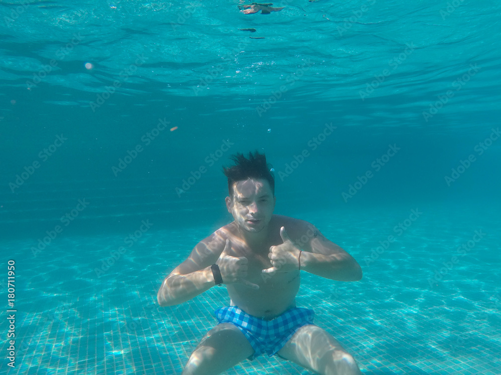 A Man floating under water in the pool with thumbs up