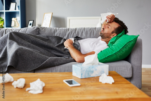 Fototapeta Sick man with fever lying on couch at home