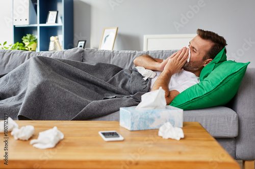 Canvas Print Sick man lying on sofa at home and blowing nose