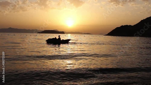 A silhouetted pedalo crosses a peaceful bay ast he sun sets over the Greek island of Kalymnos.