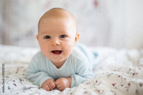 Adorable baby boy in white sunny bedroom in winter morning