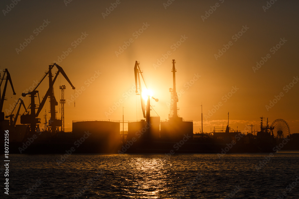 Many big cranes silhouette in the port at golden light of sunrise reflected in water. Berdiansk, Ukraine