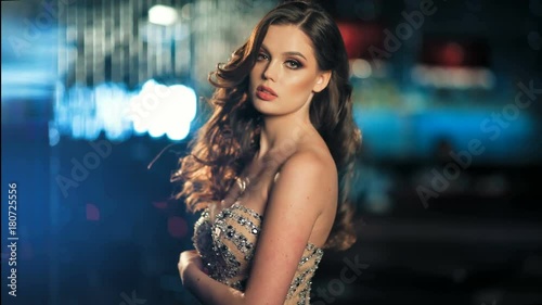 Sexy fashionable beautiful young woman in golden shining evening dress posing on night neon lights background
