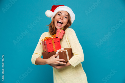 Cheerful woman in sweater and christmas hat holding gift boxes