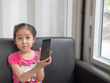 Portrait of Asia pretty little girl play mobile phone, showing the phone in her hand, near the window
