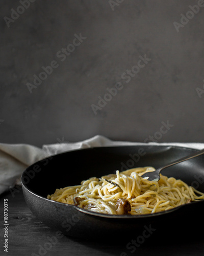 Atmospheric photo of spaghetti with shallot sauce, mushrooms, olive oil, garlic and bread crumbs. Vintage dark interior. Food photo with hands.