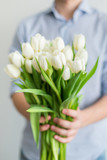 A beautiful bouquet of white tulips in the hands of a young man. A large bouquet of fresh flowers. A gift to the girl.