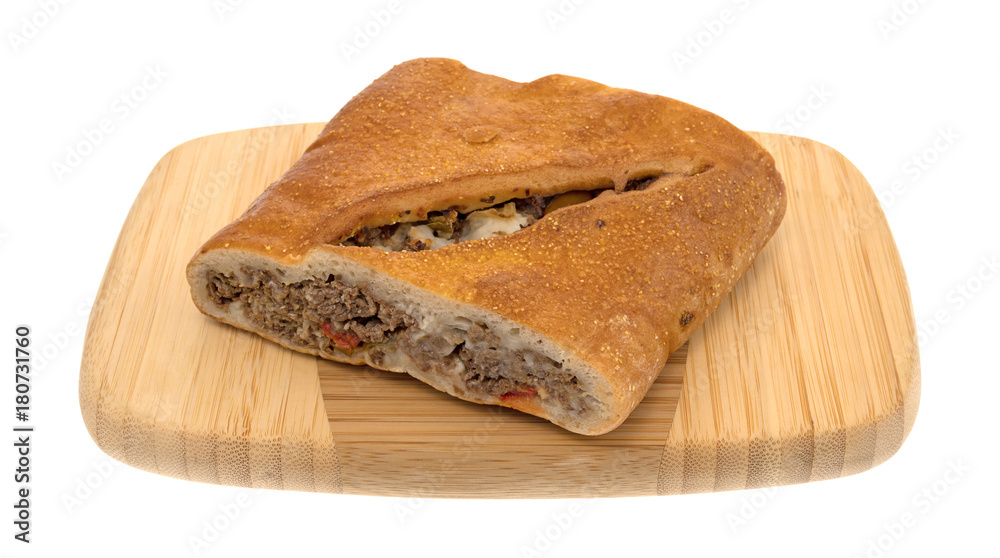 A large slice of a baked steak stromboli on a wood cutting board isolated on a white background. A large slice of a baked steak stromboli on a wood cutting board isolated on a white background.