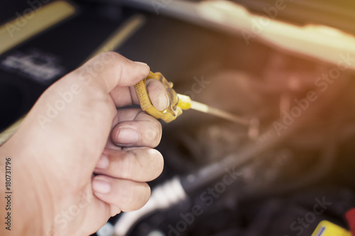 Dirty hand of mechanic has pull yellow measuring rod for checking engine oil level of a engine car. Automotive maintenance concept.