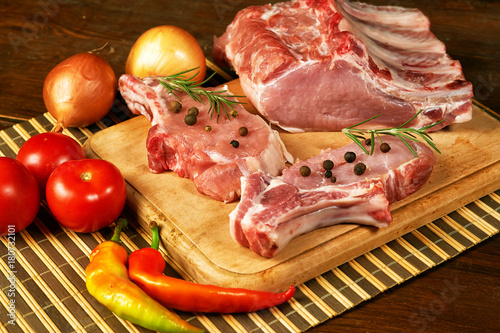 Raw steak , chops, meat with spices and vegetables on wooden table