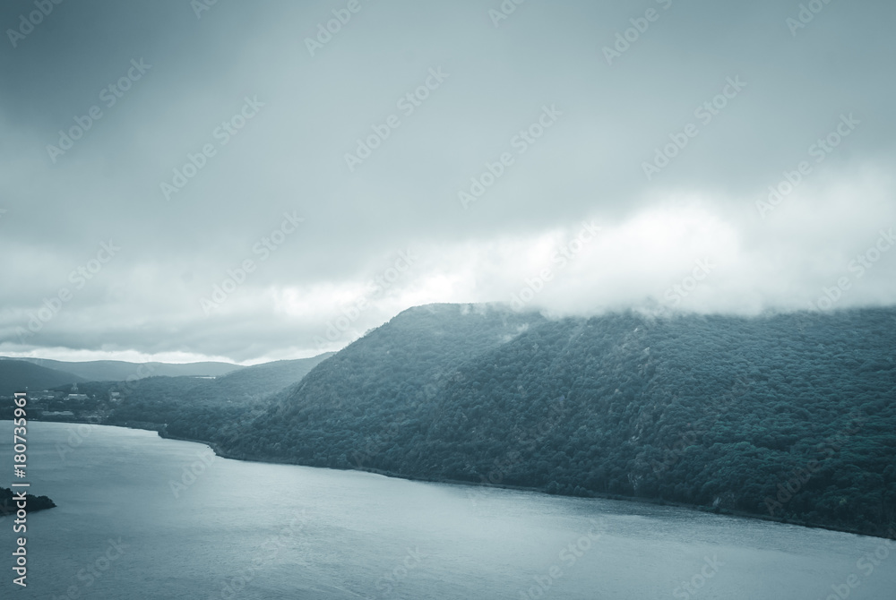Mountainside with tree foliage and mist. Misty moutain range. Clouds over mountain. Abstract nature background. River lake background.