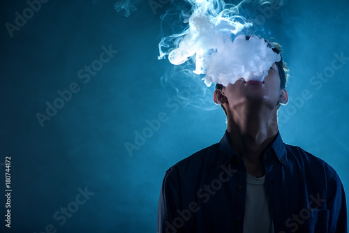 man exhales thick smoke on blue background