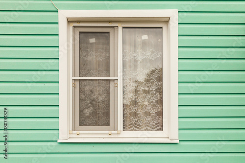 Plastic white window on the wall of the green wall house from the siding
