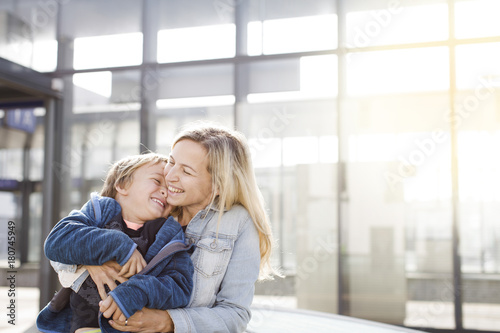 lovingly mother with happy son in casual look in front of glass building